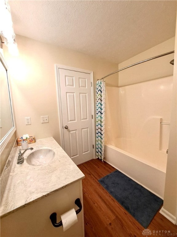 bathroom with wood-type flooring, a textured ceiling, vanity, and shower / bathtub combination with curtain