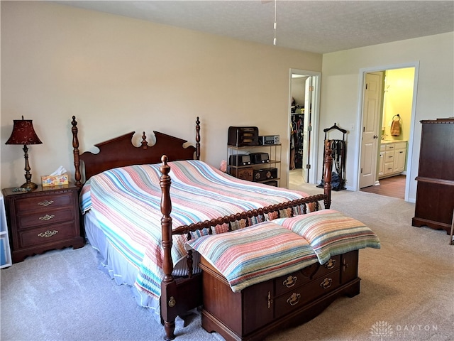 bedroom with light carpet, a textured ceiling, ensuite bath, and a spacious closet