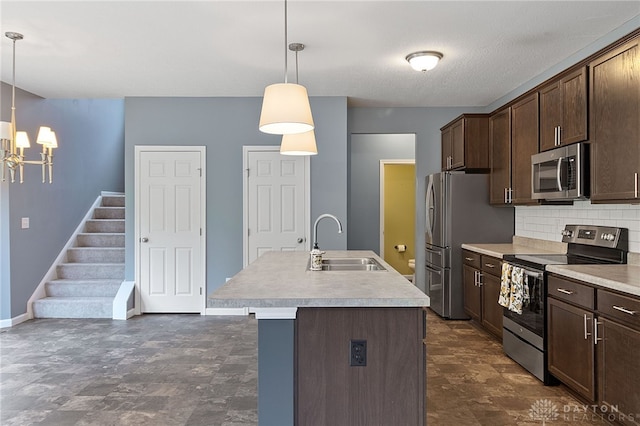 kitchen with stainless steel appliances, sink, pendant lighting, backsplash, and a kitchen island with sink