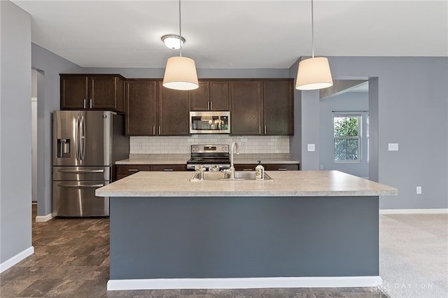 kitchen featuring appliances with stainless steel finishes, tasteful backsplash, a center island with sink, dark carpet, and decorative light fixtures