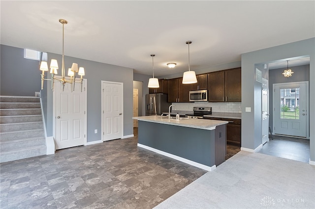 kitchen featuring appliances with stainless steel finishes, dark tile patterned floors, hanging light fixtures, backsplash, and a kitchen island with sink