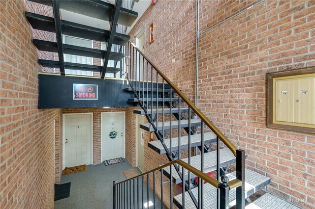 staircase with a towering ceiling, brick wall, and carpet floors