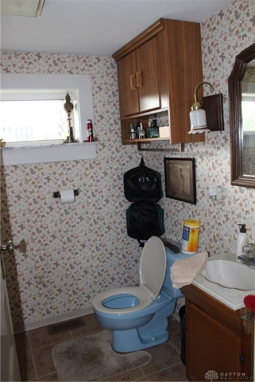 bathroom with tile patterned flooring, a healthy amount of sunlight, toilet, and vanity