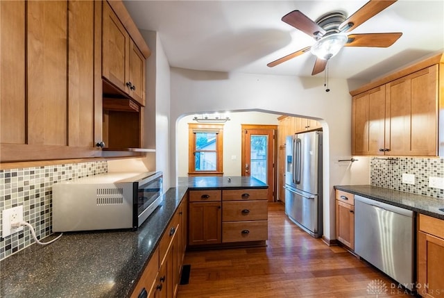 kitchen with stainless steel appliances, kitchen peninsula, ceiling fan, dark hardwood / wood-style flooring, and decorative backsplash