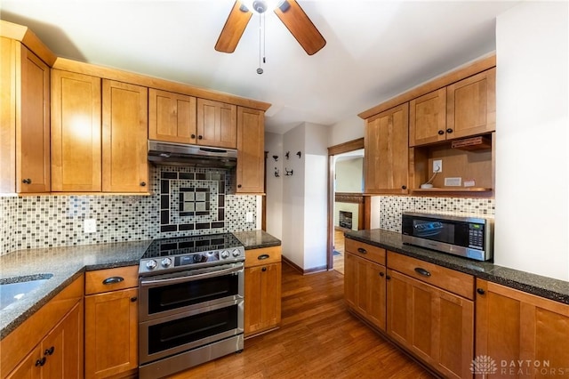 kitchen with appliances with stainless steel finishes, ceiling fan, dark stone countertops, tasteful backsplash, and dark wood-type flooring