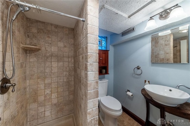 bathroom with a textured ceiling, a tile shower, sink, and toilet