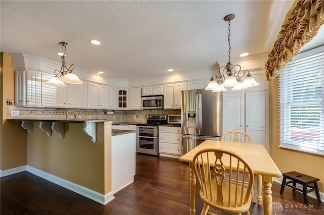 kitchen with stainless steel appliances, kitchen peninsula, hanging light fixtures, and white cabinets