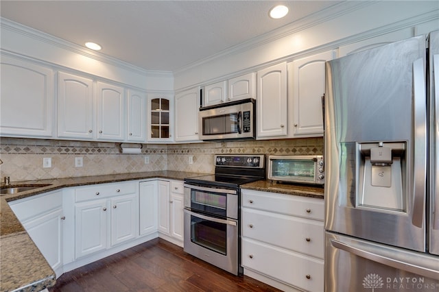 kitchen featuring appliances with stainless steel finishes, white cabinetry, sink, dark stone countertops, and dark hardwood / wood-style flooring