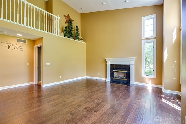 unfurnished living room featuring a tiled fireplace, a towering ceiling, and hardwood / wood-style flooring