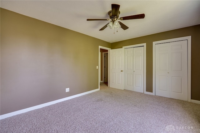 unfurnished bedroom with carpet, two closets, and ceiling fan