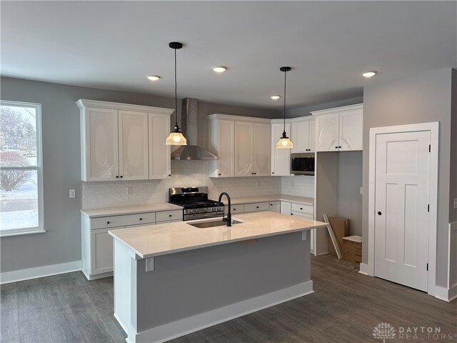 kitchen featuring an island with sink, stainless steel appliances, hanging light fixtures, wall chimney range hood, and white cabinets