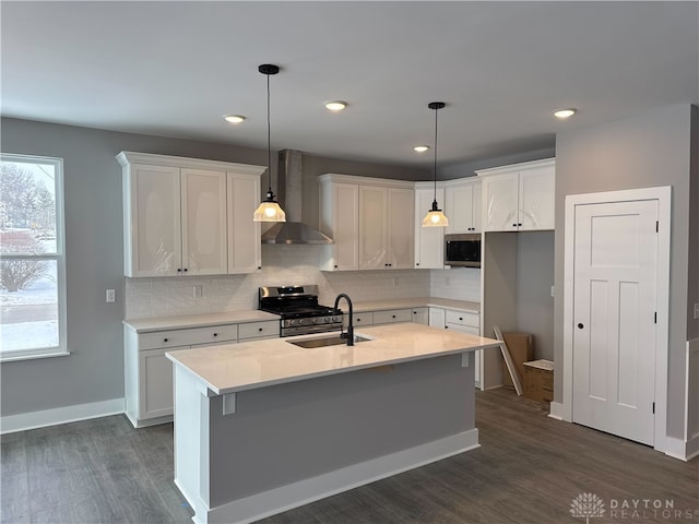 kitchen featuring white cabinetry, hanging light fixtures, a kitchen island with sink, stainless steel appliances, and wall chimney exhaust hood