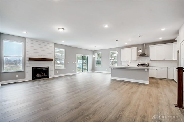 kitchen with wall chimney exhaust hood, a kitchen island with sink, white cabinets, and decorative light fixtures