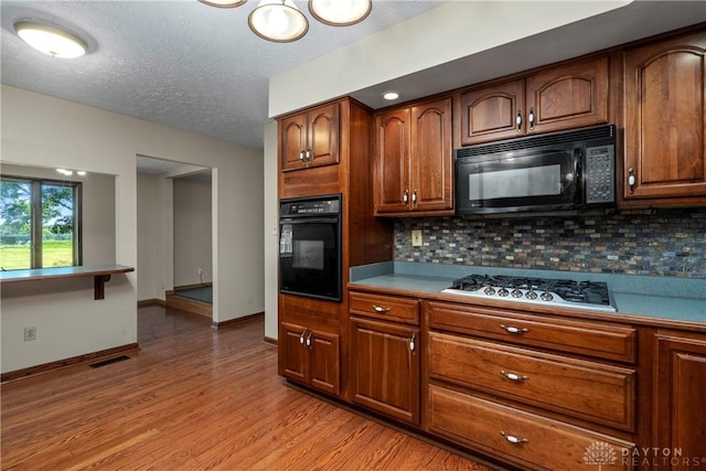 kitchen featuring tasteful backsplash, light hardwood / wood-style flooring, black appliances, and a textured ceiling