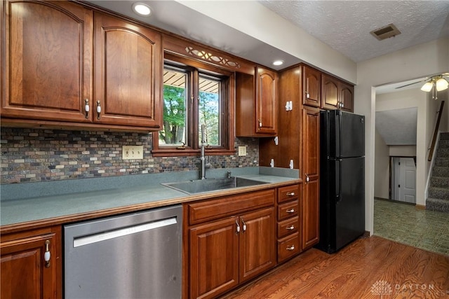 kitchen featuring sink, black fridge, light wood-type flooring, stainless steel dishwasher, and backsplash