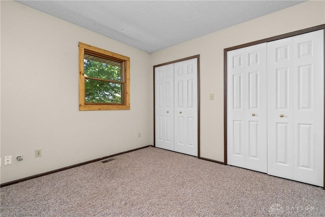 unfurnished bedroom with a textured ceiling, light carpet, and two closets