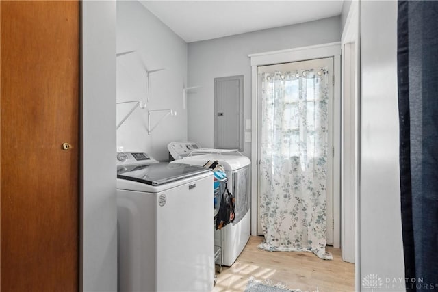 clothes washing area featuring electric panel, separate washer and dryer, and light hardwood / wood-style floors