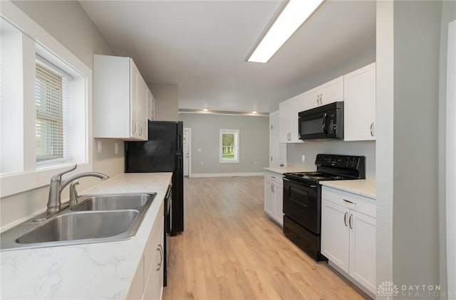 kitchen featuring sink, a healthy amount of sunlight, white cabinets, black appliances, and light wood-type flooring