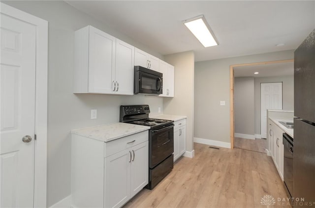 kitchen with black appliances, white cabinets, sink, light hardwood / wood-style flooring, and light stone counters