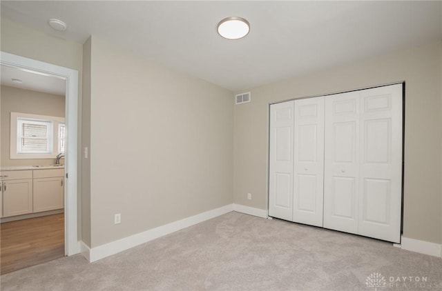 unfurnished bedroom with a closet, light colored carpet, and sink