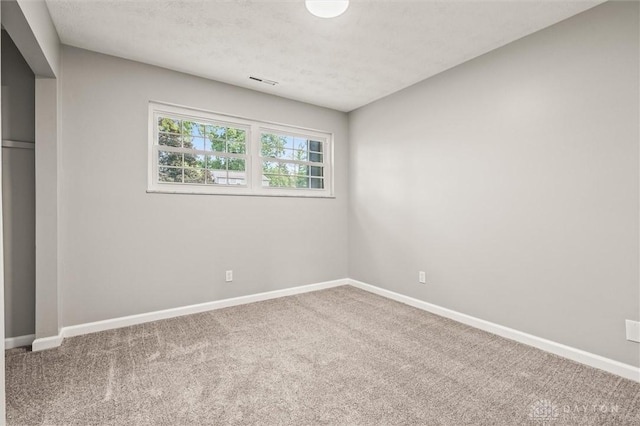 spare room with a textured ceiling, carpet floors, visible vents, and baseboards