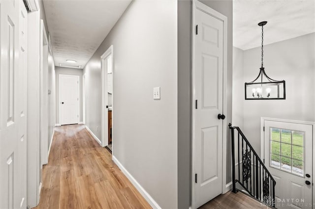 hall with a chandelier, light wood-type flooring, an upstairs landing, and baseboards