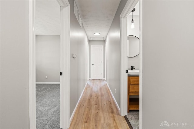 hall with light wood-style flooring, light carpet, a sink, visible vents, and baseboards