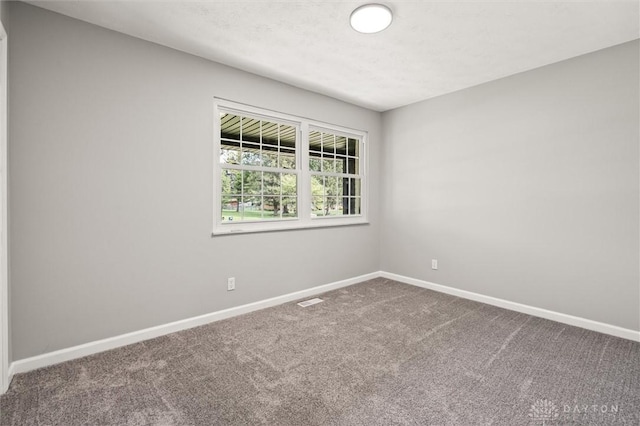 empty room with carpet, visible vents, and baseboards