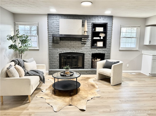 living area featuring light wood-style floors, plenty of natural light, a fireplace, and baseboards