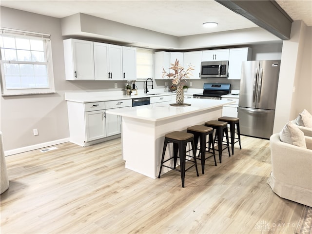 kitchen featuring a breakfast bar area, stainless steel appliances, white cabinets, light countertops, and light wood-type flooring