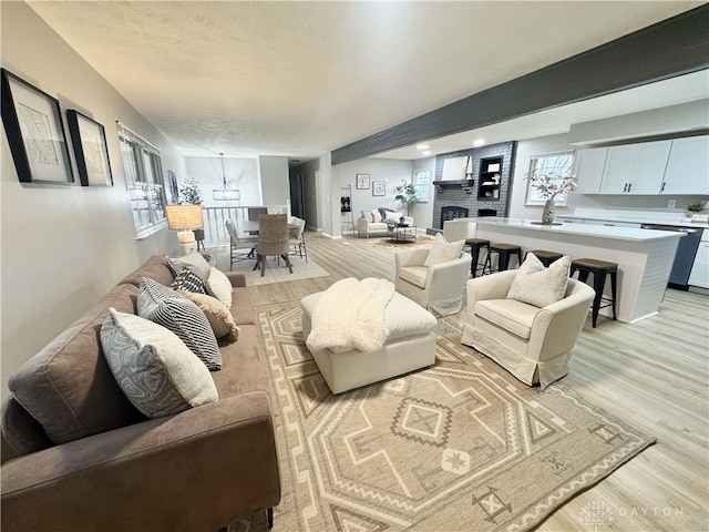 living area with a textured ceiling, light wood finished floors, and a brick fireplace