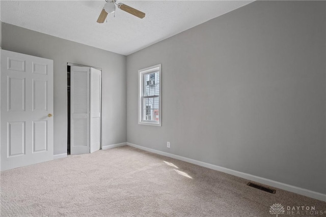 unfurnished bedroom with ceiling fan, light colored carpet, a closet, and a textured ceiling