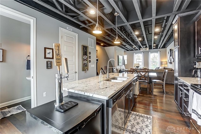 kitchen with pendant lighting, sink, dark brown cabinets, light stone counters, and an island with sink