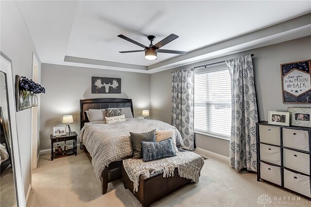 bedroom with light carpet, ceiling fan, and a tray ceiling