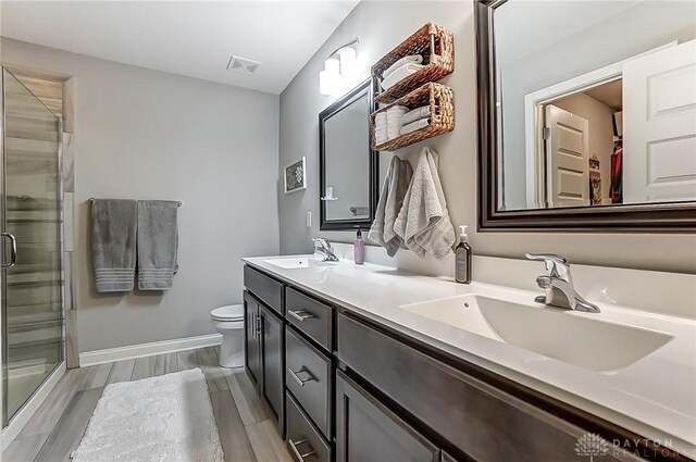 bathroom featuring toilet, a shower with door, and double vanity