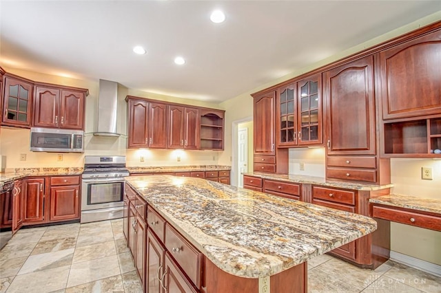 kitchen with light tile patterned flooring, wall chimney range hood, light stone countertops, a kitchen island, and appliances with stainless steel finishes