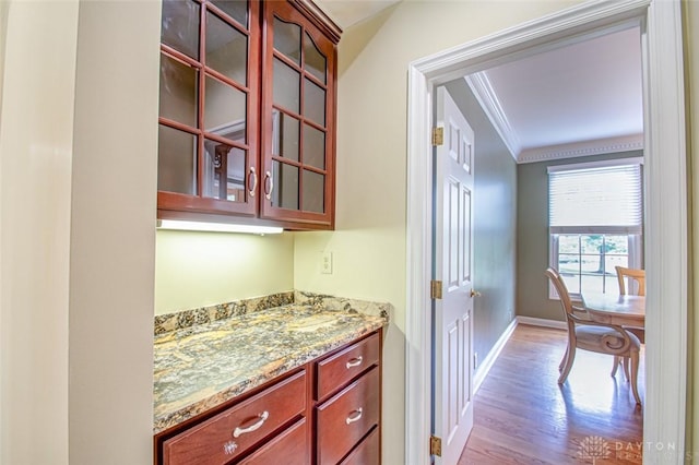 bar with light stone countertops, light hardwood / wood-style flooring, and ornamental molding