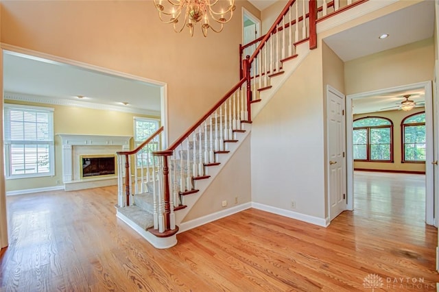 staircase with light hardwood / wood-style floors, a fireplace, ceiling fan with notable chandelier, and a towering ceiling