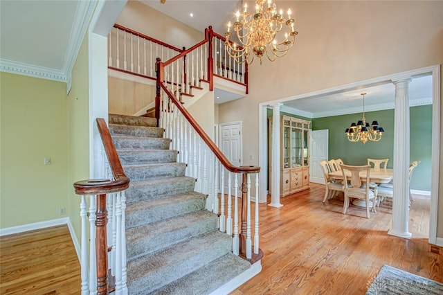 stairs featuring decorative columns, ornamental molding, light wood-type flooring, and an inviting chandelier