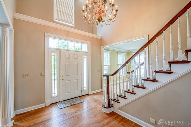 entrance foyer with crown molding, decorative columns, an inviting chandelier, a high ceiling, and wood-type flooring