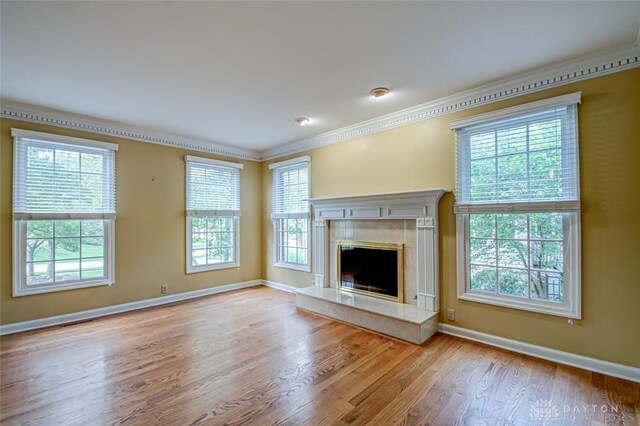 unfurnished living room with a premium fireplace, crown molding, light hardwood / wood-style flooring, and a healthy amount of sunlight