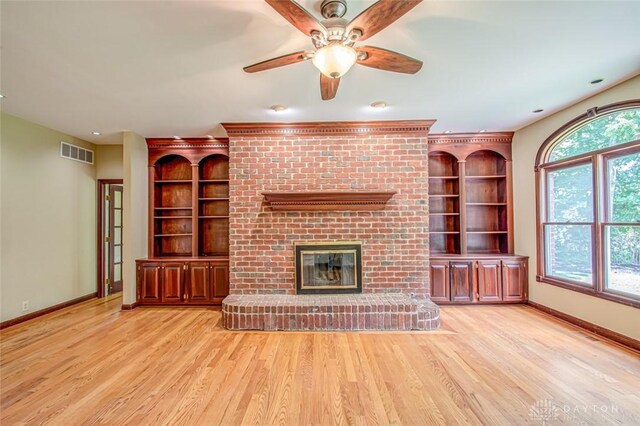 unfurnished living room featuring built in features, a fireplace, ceiling fan, and light wood-type flooring