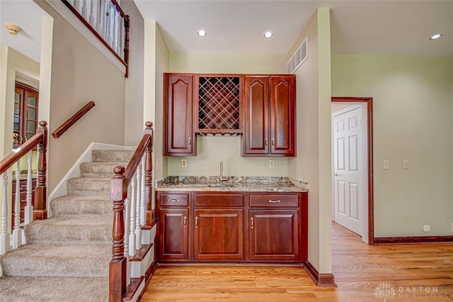 bar featuring light hardwood / wood-style floors, light stone counters, and sink