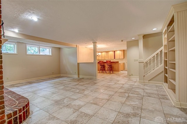 unfurnished living room with a textured ceiling, bar, decorative columns, and light tile patterned floors