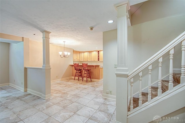 kitchen with light tile patterned flooring, a chandelier, pendant lighting, a kitchen bar, and ornate columns