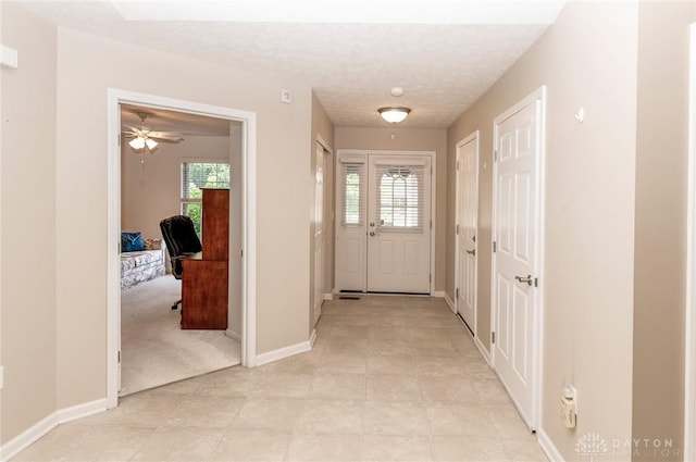 doorway featuring ceiling fan, light carpet, and a textured ceiling