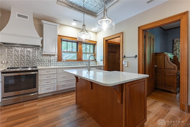 kitchen with a kitchen island with sink, stainless steel stove, light wood-type flooring, and premium range hood