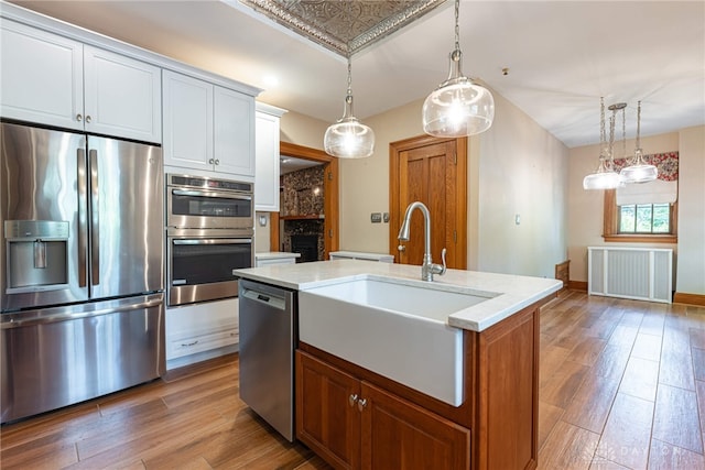 kitchen with sink, appliances with stainless steel finishes, hardwood / wood-style flooring, an island with sink, and pendant lighting