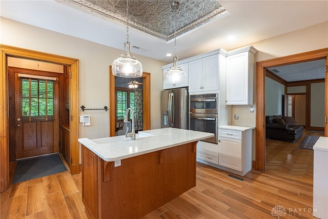 kitchen featuring decorative light fixtures, light stone countertops, a kitchen island with sink, stainless steel appliances, and white cabinets