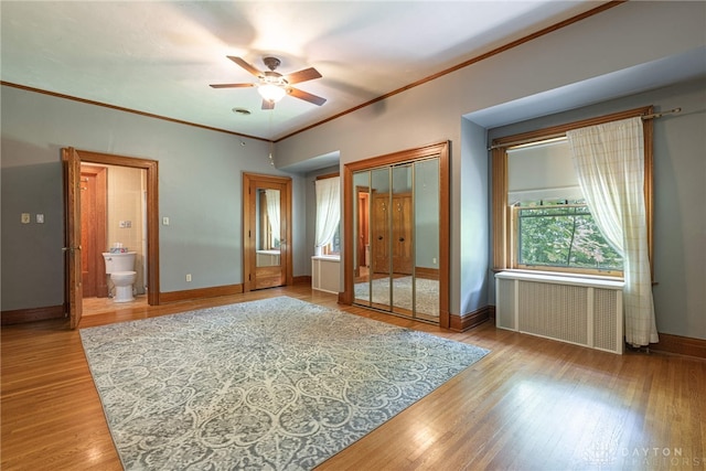 unfurnished bedroom featuring ceiling fan, wood-type flooring, radiator, a closet, and connected bathroom